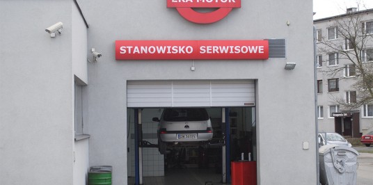 Brama wjazdowa a za nią pojazd na podnośniku w trakcie kontroli. Zaufaj nam i przyjedź do Wrocławia na ulicę Strzegomską.